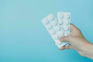 Hand holding a blister pack of medicine pill on blue background photo