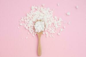 Sea salt in a wooden spoon on pink background photo