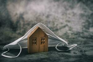 Wooden house model with hygiene face mask on dark background photo