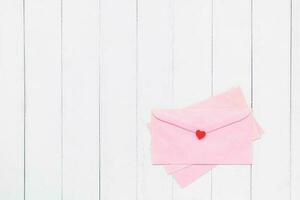 Flat lay of pink envelope with red heart on white table background photo