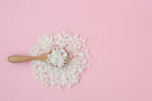 Sea salt in a wooden spoon on pink background photo