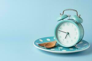 An alarm clock on an empty plate and cutlery set against blue background photo