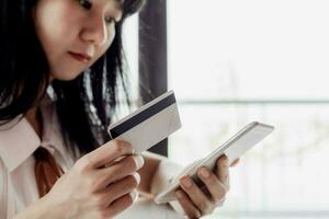 asiático mujer participación un crédito tarjeta y utilizando teléfono inteligente foto