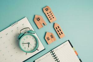 An alarm clock with calendar, notebook and wooden house model photo