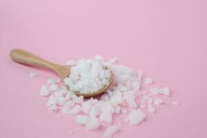 Sea salt in a wooden spoon on pink background photo