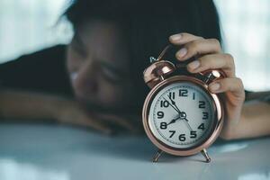 The lazy asian woman lay down on the table and reached out to turn off the alarm clock photo