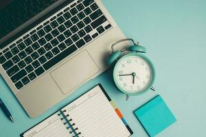 ordenador portátil con un alarma reloj, un diario cuaderno y otros trabajo y educativo materiales foto