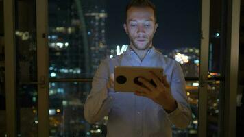 a man is using his tablet at night inside modern city apartment with skyline view video