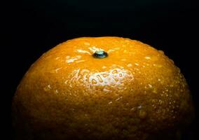 Gota de agua sobre la superficie brillante de frescura naranja sobre fondo negro foto