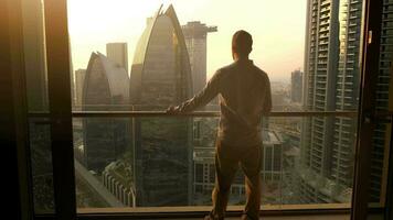 Young Business Man Standing on Balcony of Modern High Rise Apartment Overlooking Futuristic Cityscape Skyline video