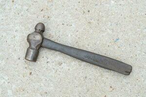 Single dirty old metal or iron hammer with wooden handle laying down on concrete floor. Flat lay photo