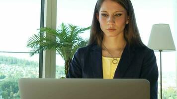 une femme dans des lunettes est à la recherche à sa portable travail à l'intérieur moderne Bureau video