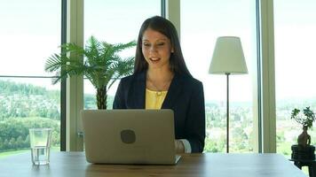 un mujer en lentes es mirando a su ordenador portátil trabajando dentro moderno oficina video