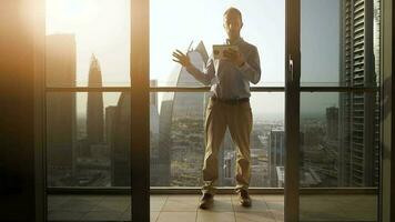 Young Business Man Standing on Balcony of Modern High Rise Apartment Overlooking Futuristic Cityscape Skyline video