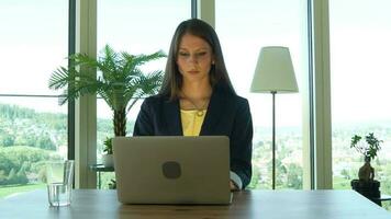 une femme dans des lunettes est à la recherche à sa portable travail à l'intérieur moderne Bureau video