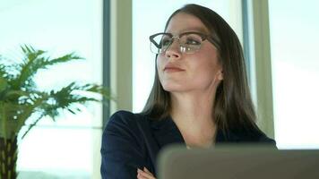 a woman in glasses is looking at her laptop working inside modern office video