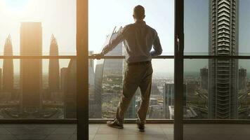 jong bedrijf Mens staand Aan balkon van modern hoog stijgen appartement met uitzicht futuristische stadsgezicht horizon video