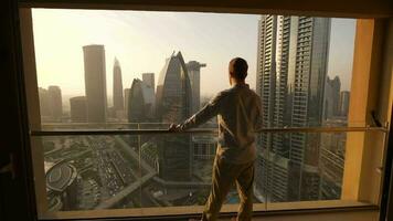 Young Business Man Standing on Balcony of Modern High Rise Apartment Overlooking Futuristic Cityscape Skyline video