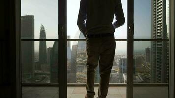 joven negocio hombre en pie en balcón de moderno alto subir Departamento con vista a futurista paisaje urbano horizonte video