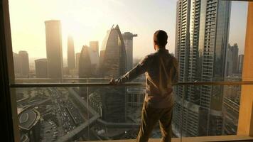 jong bedrijf Mens staand Aan balkon van modern hoog stijgen appartement met uitzicht futuristische stadsgezicht horizon video
