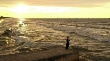 Young elegant woman dancing with hands up holding black scarf on the pier in sunset time. Summertime, vacation, freedom concept video