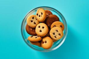 A glass bowl filled with chocolate chip cookies on a solid color background. photo