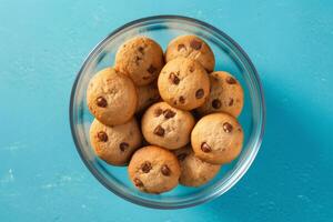 A glass bowl filled with chocolate chip cookies on a solid color background. photo