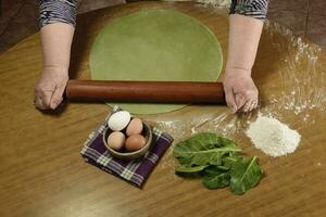 Grandma's hands kneading, dough for green noodles. photo