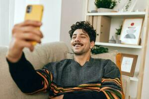 Sitting man phone typing businessman indoor selfie message lifestyle home freelance communication technology sofa photo