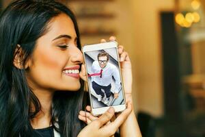 Online dating young indian woman holding her phone with photo of her beloved one