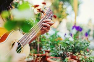 Faceless photo of a woman playing ukulele in the garden, focus on the hand