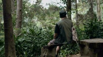 an Asian man in a black hat is sitting on a wooden chair while enjoying the scenery video