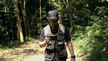 un asiático hombre es caminando mientras mirando a su inteligente teléfono en el medio de el bosque video