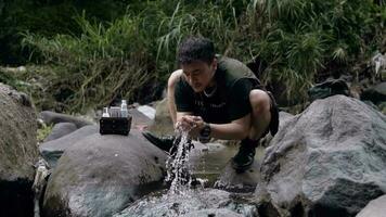 an Asian man is washing his face with river water between big rocks video