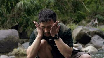 an Asian man is washing his face with river water between big rocks video