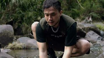 an Asian man in a black shirt is washing his face by the river in a forest video