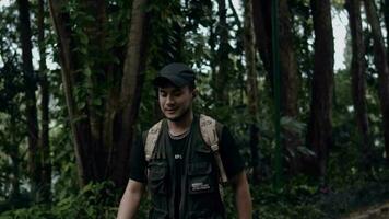 un asiatique homme dans une noir chapeau en marchant tandis que explorant une forêt dans le montagnes video