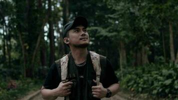ein asiatisch Mann im ein schwarz Hut Gehen während erkunden ein Wald im das Berge video