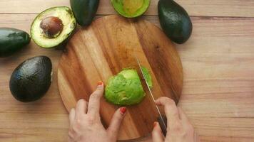 top view of young woman hand cutting slice of avocado on wooden table video