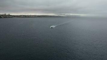 POV aerial drone view tracking a speeding yacht on a bay during a cloudy day - captured in Cascais, Portugal video