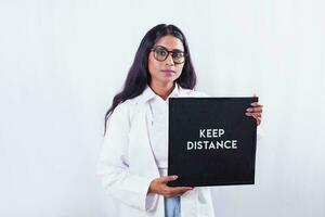 a woman in a lab coat holding a sign that says keep distance photo