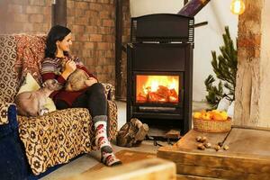 A young caucasian smiling woman sitting near a fireplace with her pets on a sofa photo