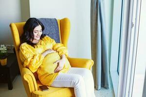 Young pregnant Indian woman sitting in armchair at home photo