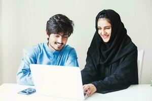 a young man and woman in hijab are looking at a laptop photo