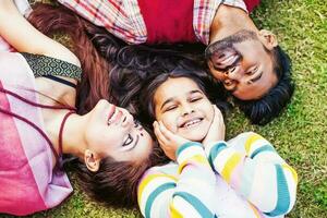 Closeup portrait of Indian family of three mother, father and cute little daughter, lying down on a grass photo