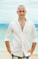 a bald man in a white shirt standing on the beach photo