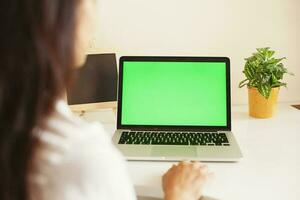 a woman is working on a laptop with a green screen photo