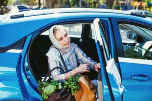 musulmán mujer en un azul coche con un compras bolso foto