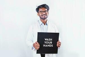 Young man in doctor uniform holding a sign Wash your hands over white background photo