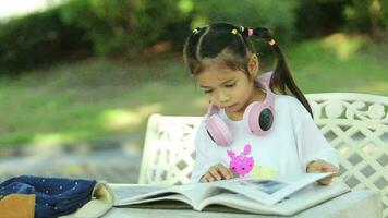 feliz ásia menina lendo livro dentro a jardim. Educação conceito. video